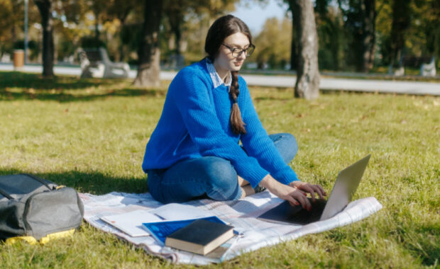 A student writing on a laptop computer outside