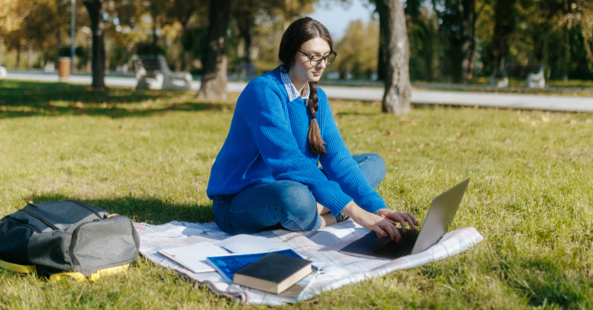 A student writing on a laptop computer outside
