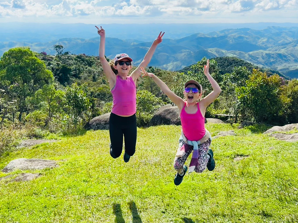 Two girls jumping with a mountain behind them