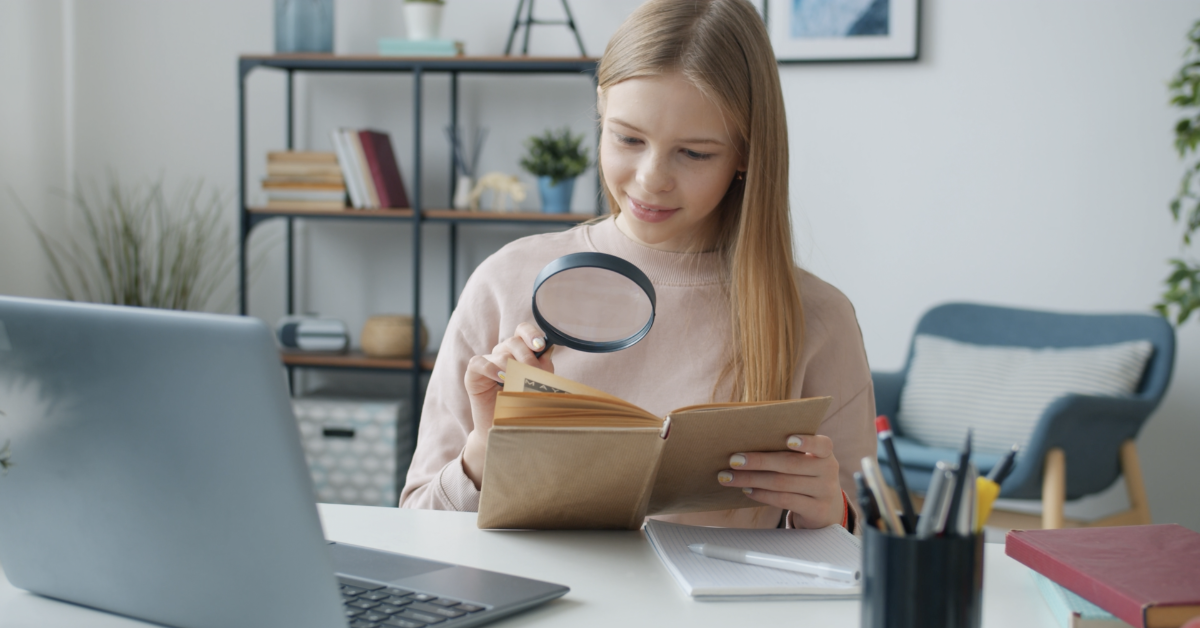 A student reading a page in a book with a magnifying glass