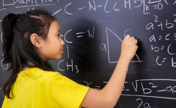A students writes math equations on a chalkboard